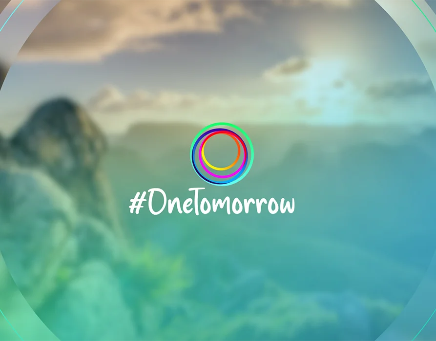 Im Vordergrund: Logo bestehend aus Schriftzug #OneTomorrow und bunten Kreisen. Im Hintergrund: Verschwommenes Bild einer alpinen Landschaft mit Sonnenuntergang. (Foto)